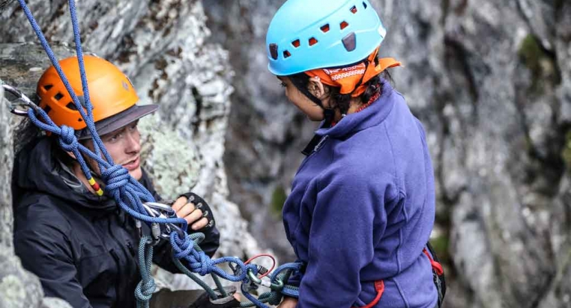 an instructor gives direction to a student preparing to rock climb on an outward bound trip in north carolina